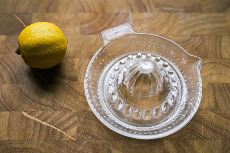 Glass lemon squeezer with a lemon on wooden background.
