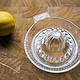 Glass lemon squeezer with a lemon on wooden background.