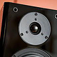 A black, high quality loudspeaker box against a colored background.